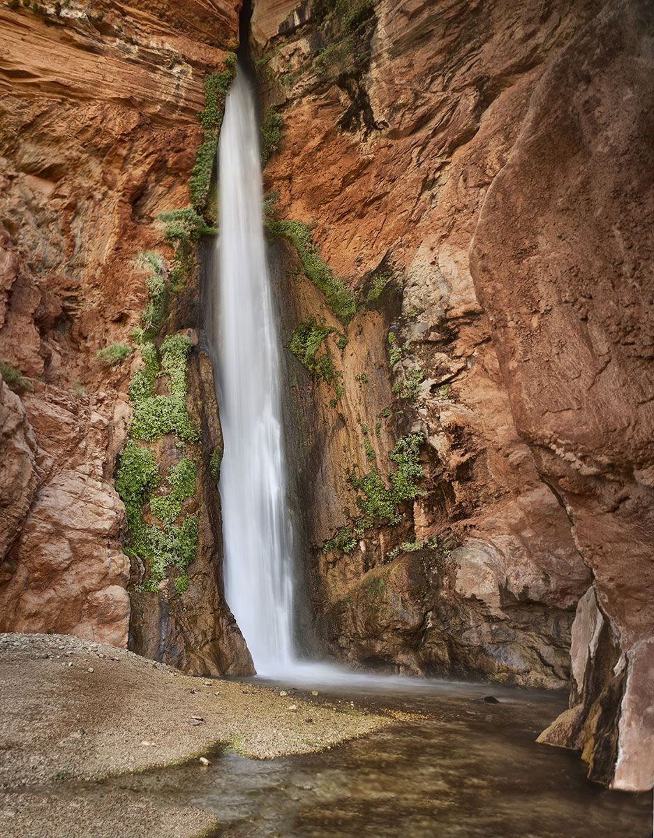 A waterfall is surrounded by rocks and plants in a canyon.