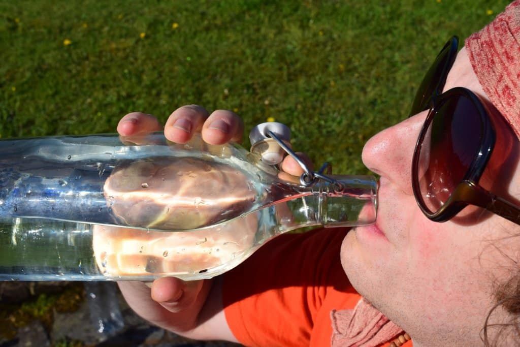 A man wearing sunglasses is drinking water from a bottle.