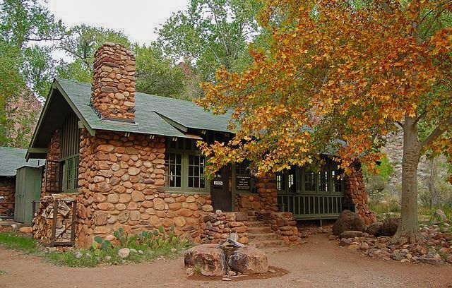 A small stone house with a green roof is surrounded by trees