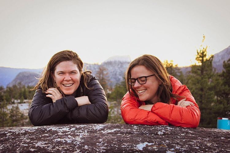 Two women are laying on a rock with their arms crossed and smiling.