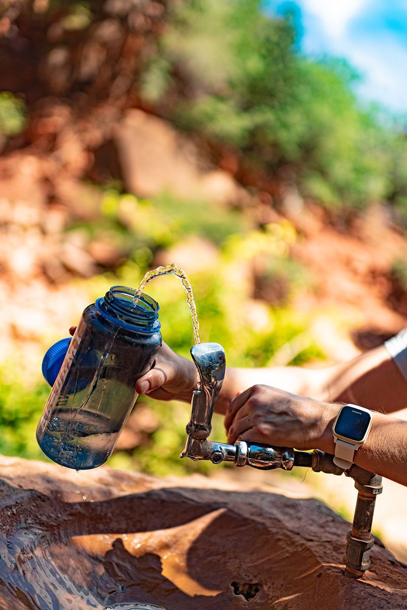 A person is pouring water from a bottle into a faucet.