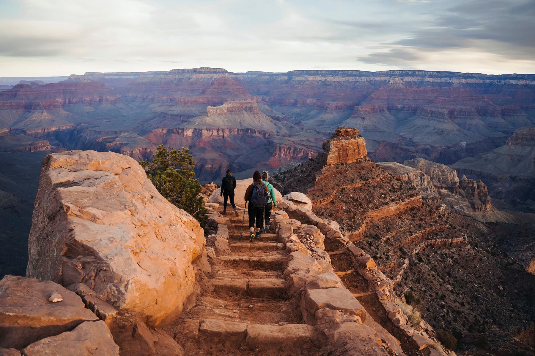 People walking along a stone path on the rim of the Grand Canyon at dusk.