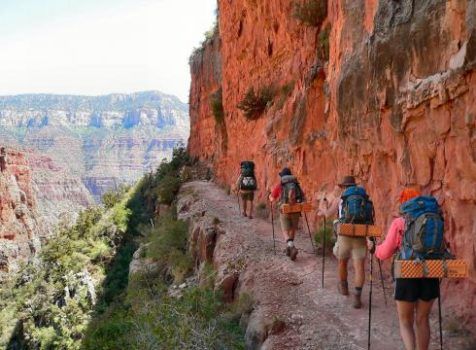 A group of people are hiking down a trail next to a cliff.