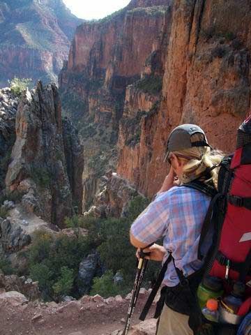 A woman with a backpack is standing on top of a mountain.