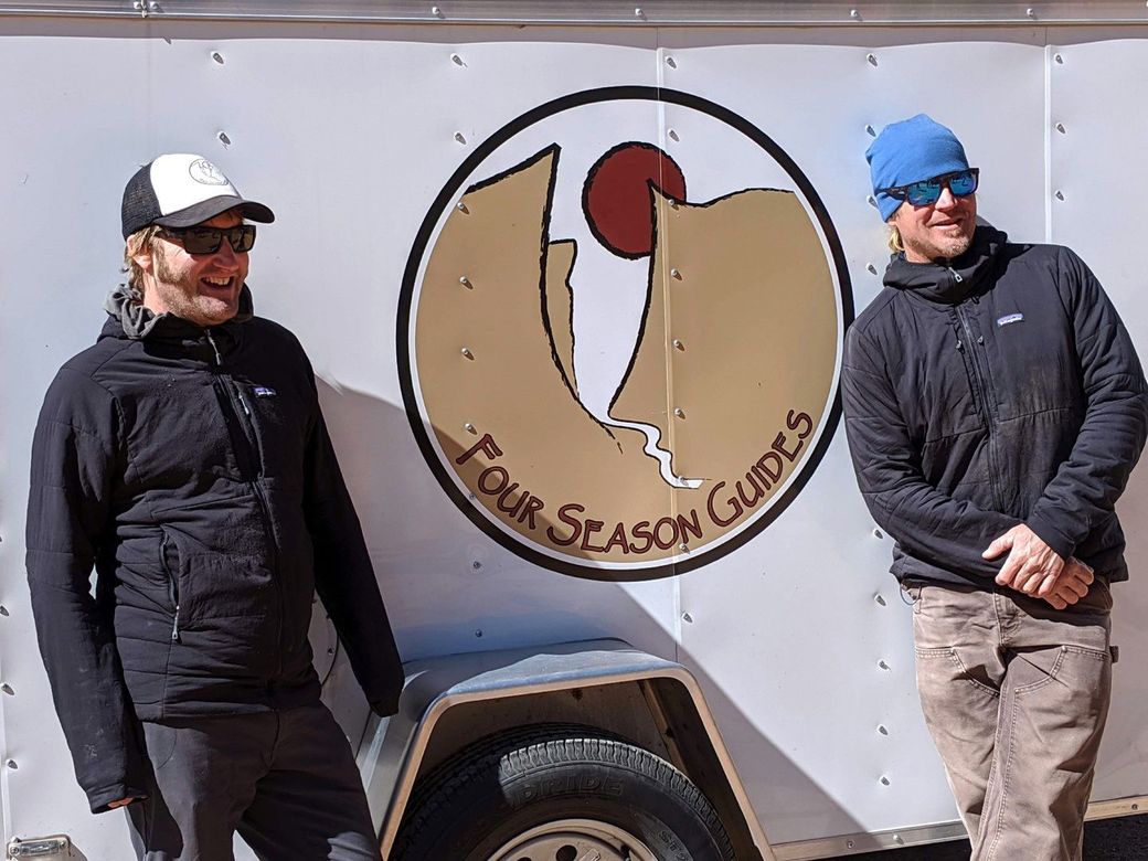 Two men are standing in front of a trailer that says four season guides