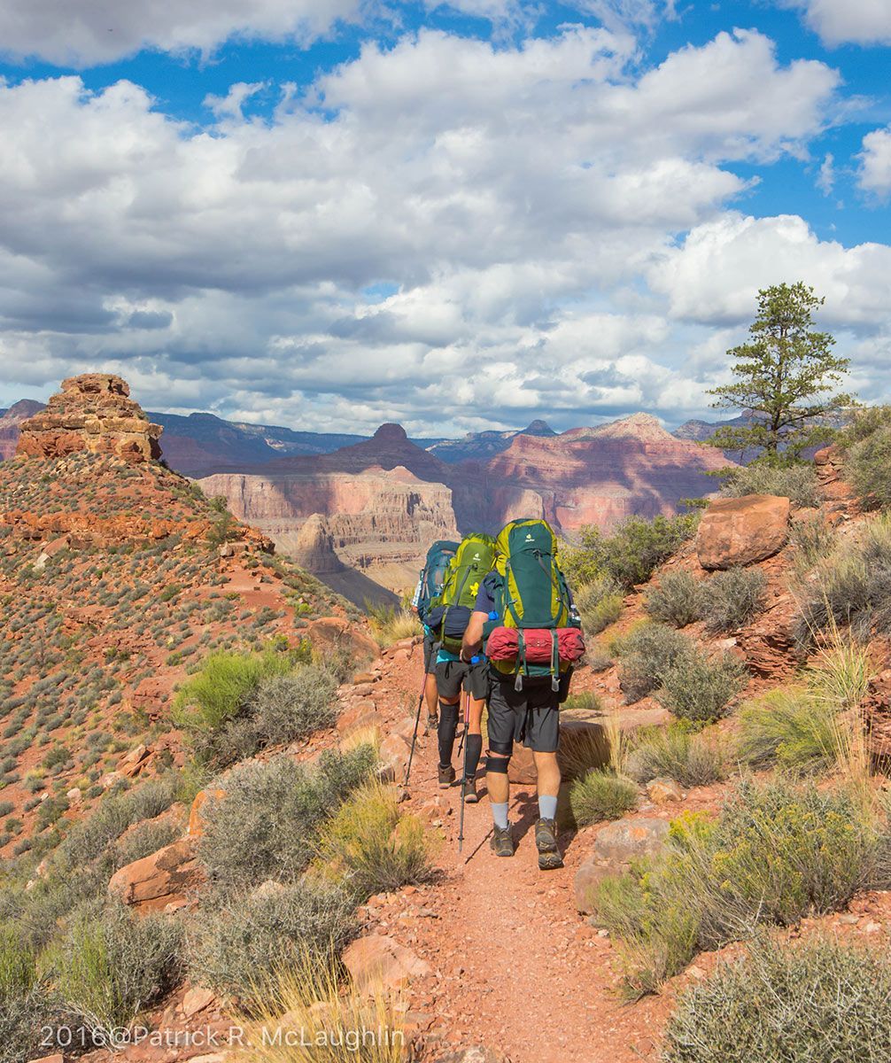 People wearing backpacks hike toward a canyon