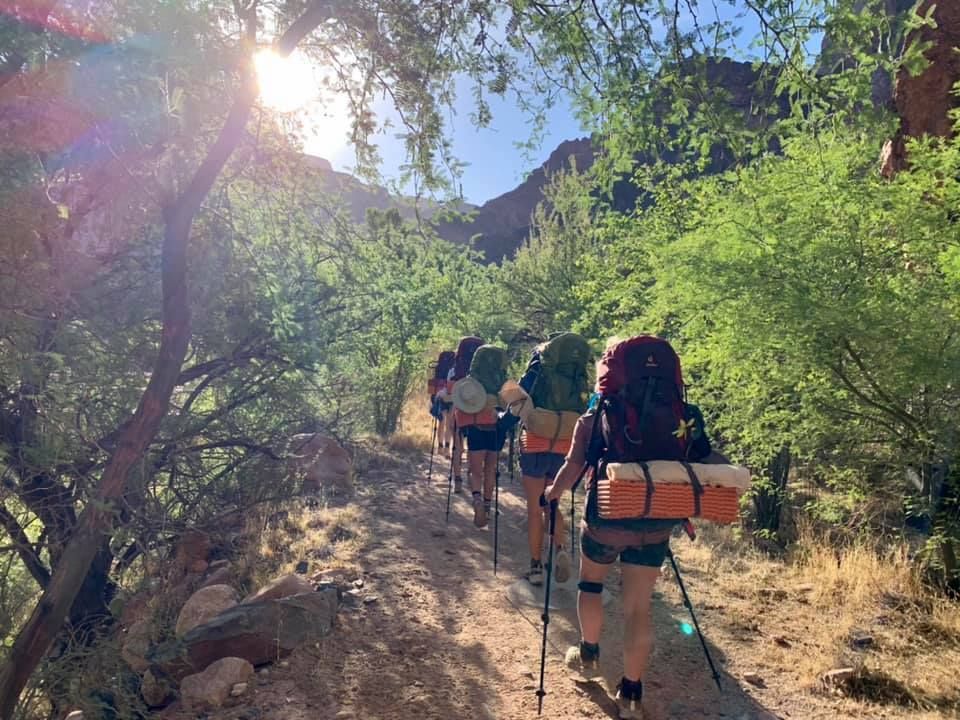 A group of people with backpacks are hiking down a dirt path.