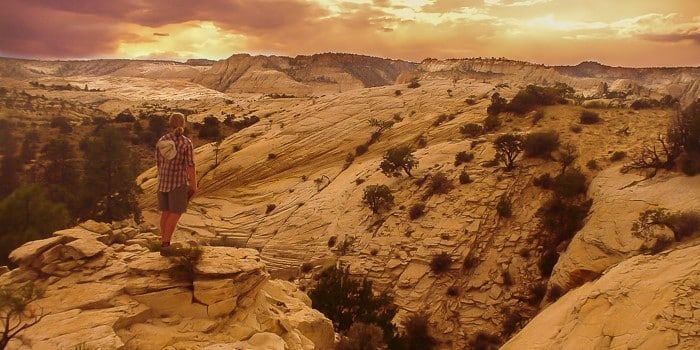 A person is standing on top of a rocky cliff in the desert.