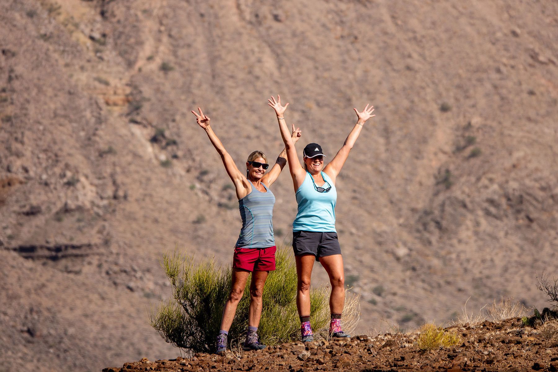 Two women are standing on top of a hill with their arms in the air.