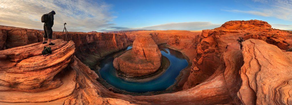 A person on a cliff overlooks Horseshoe Bend, a river shaped like a horseshoe in a red rock canyon.