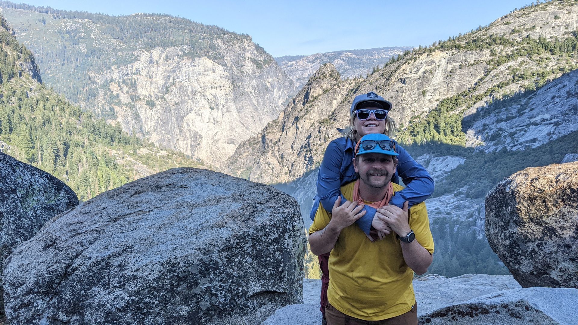 A man is carrying a woman on his shoulders in the mountains.