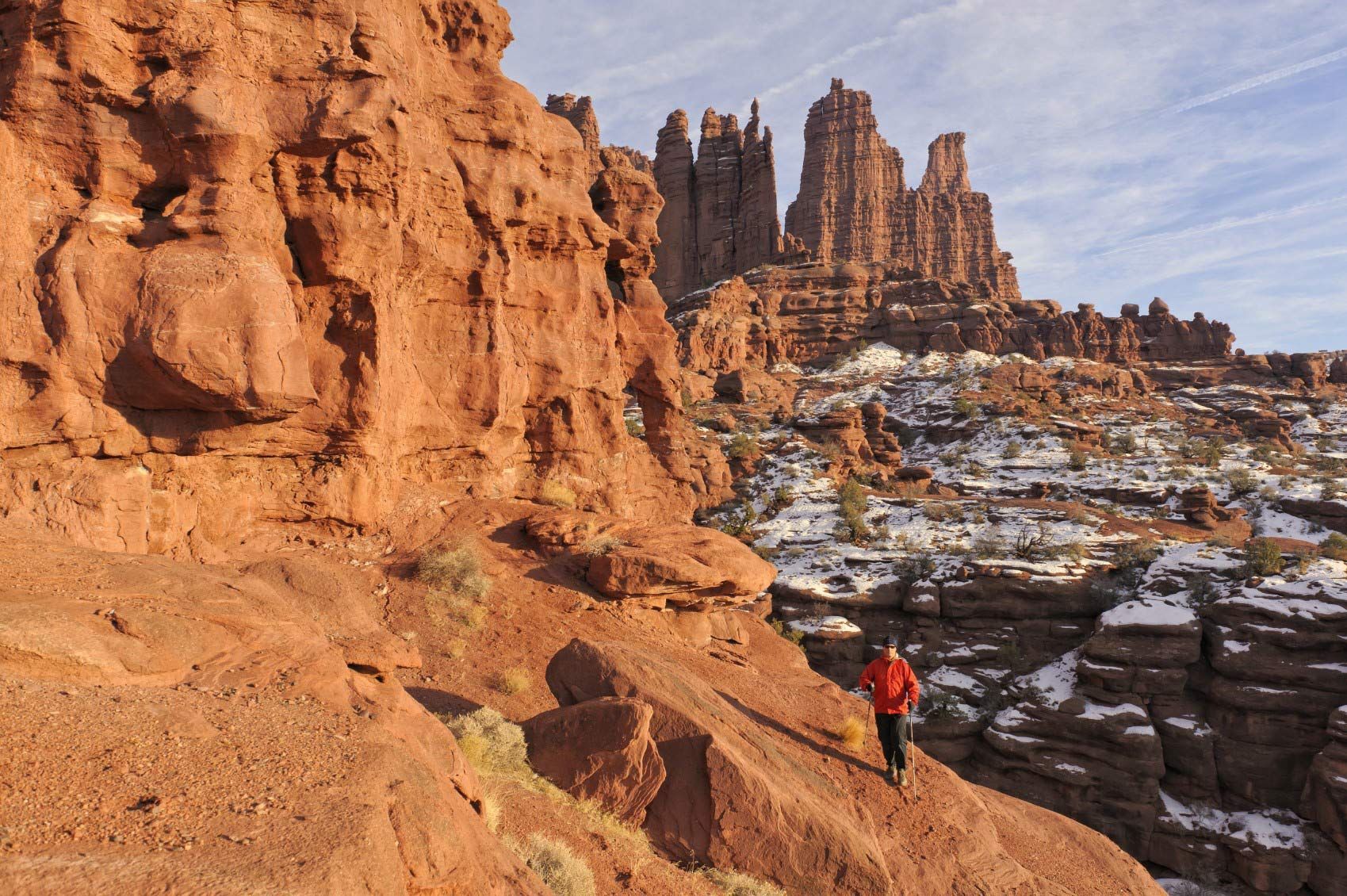 A man in a red jacket is standing on top of a rocky cliff.