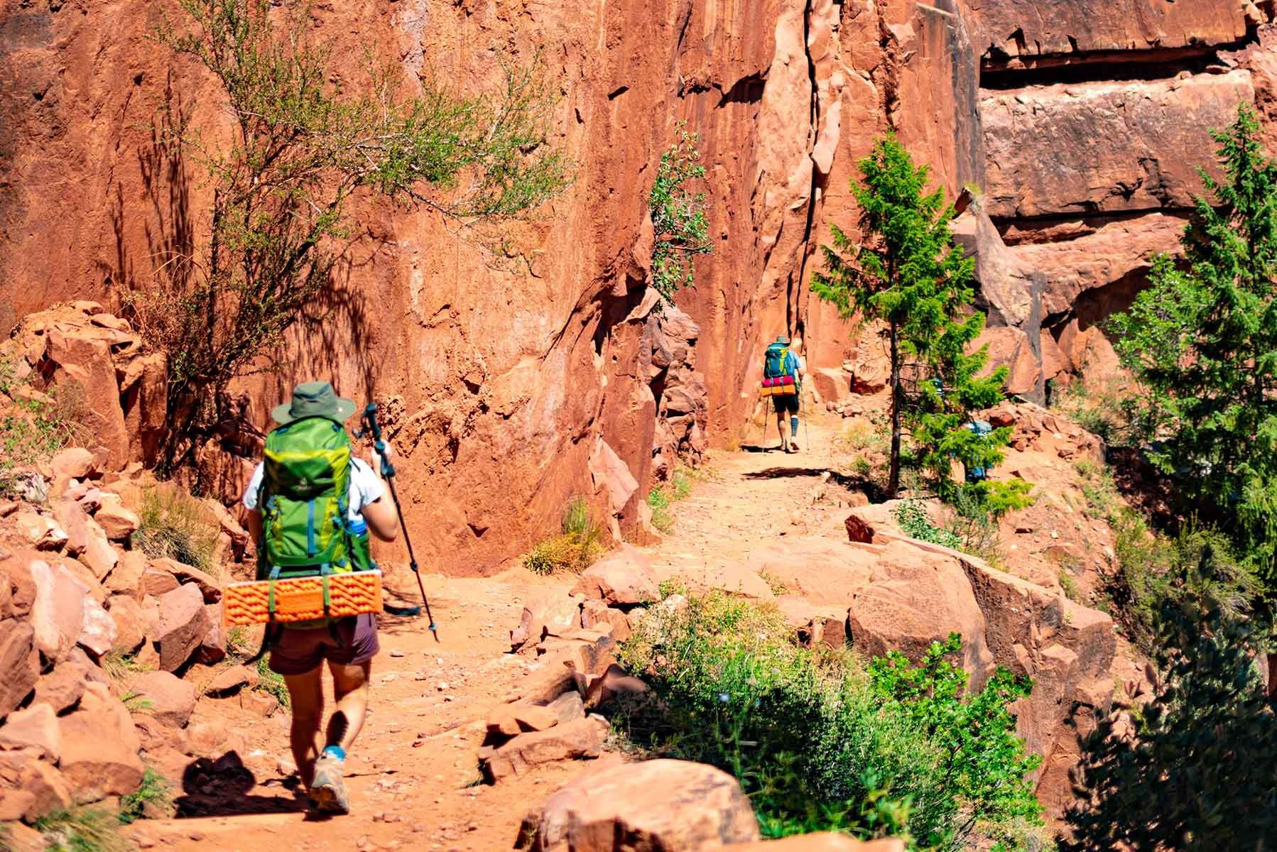 Two people wearing backpacks hike through orange canyons