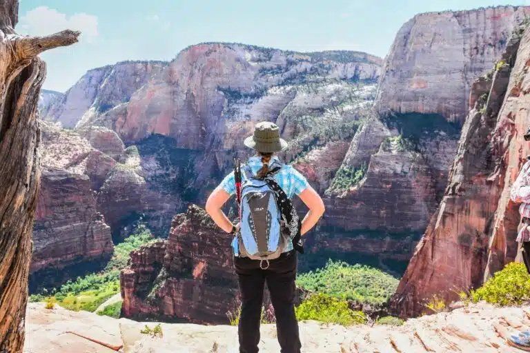 A woman with a backpack is standing on top of a mountain.