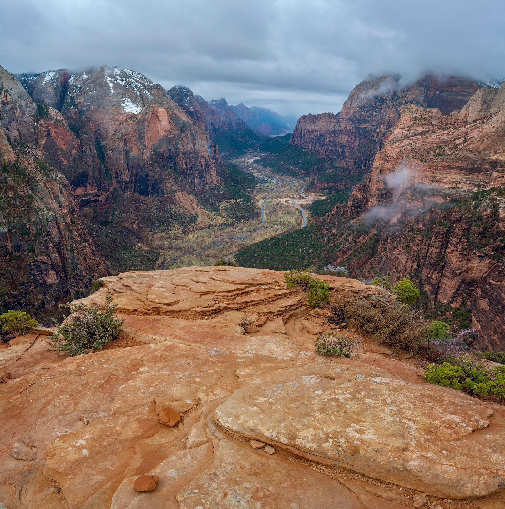 Rocky canyon overlook with red cliffs, a winding river, and low clouds