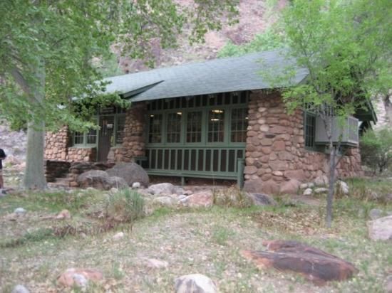 A stone cabin with a green roof is surrounded by trees and grass.