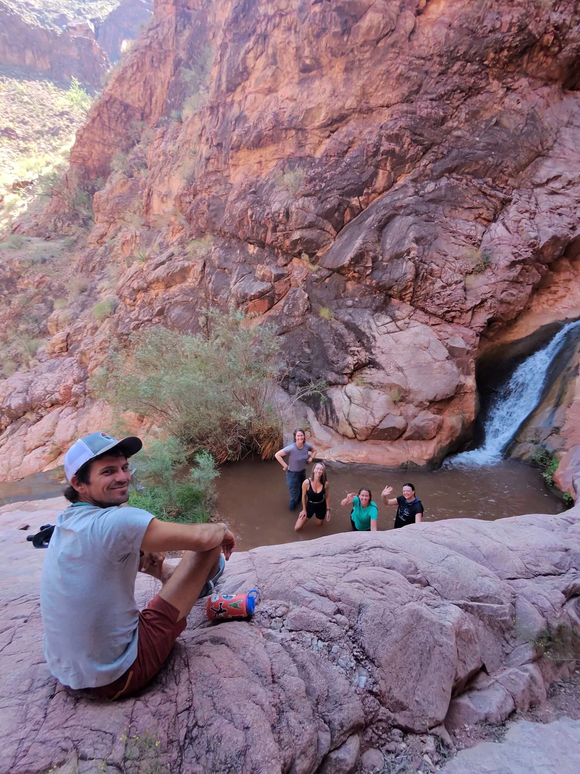 A man is sitting on a rock next to a waterfall.