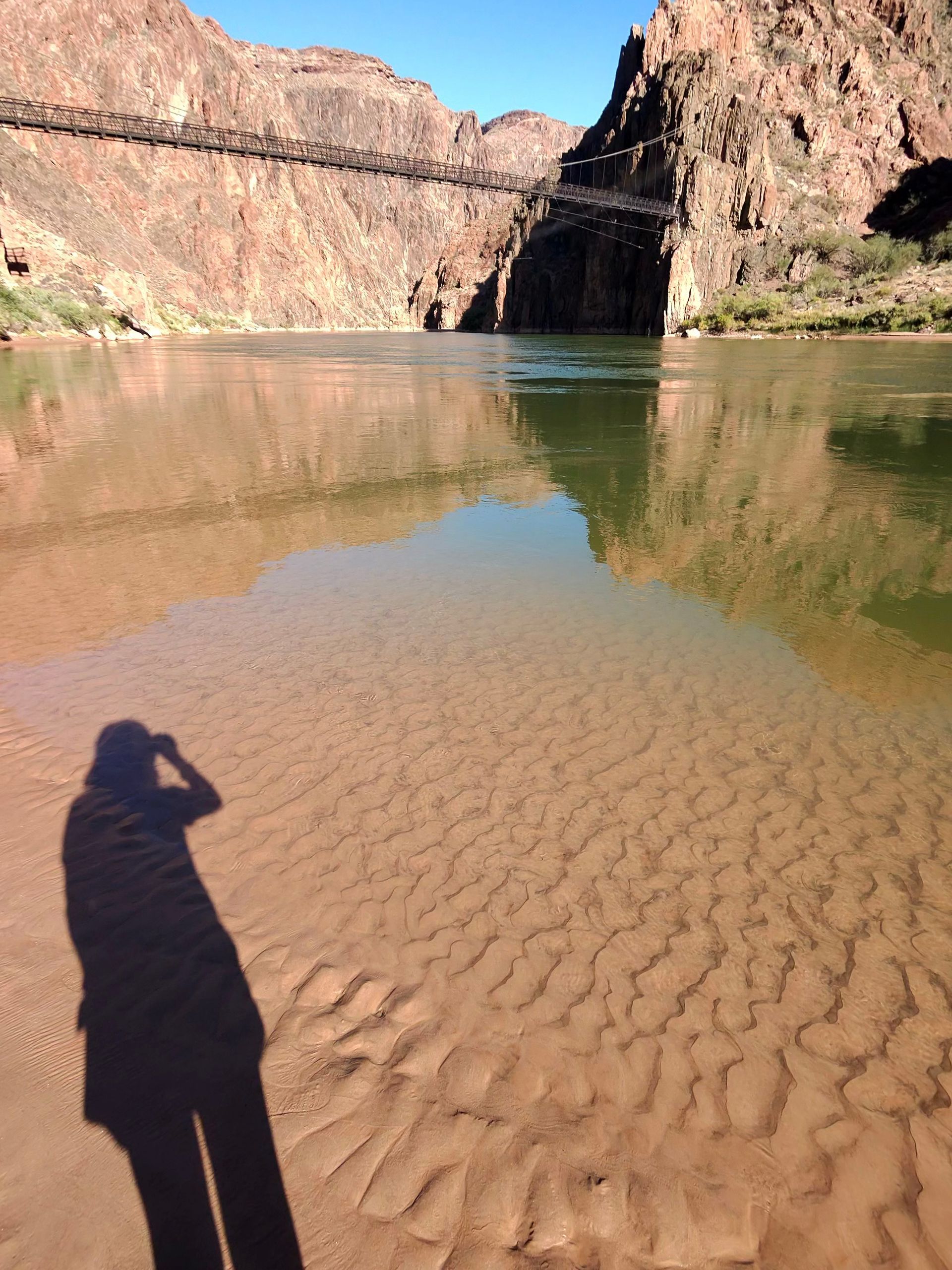 A shadow of a person is cast on the sand near a body of water