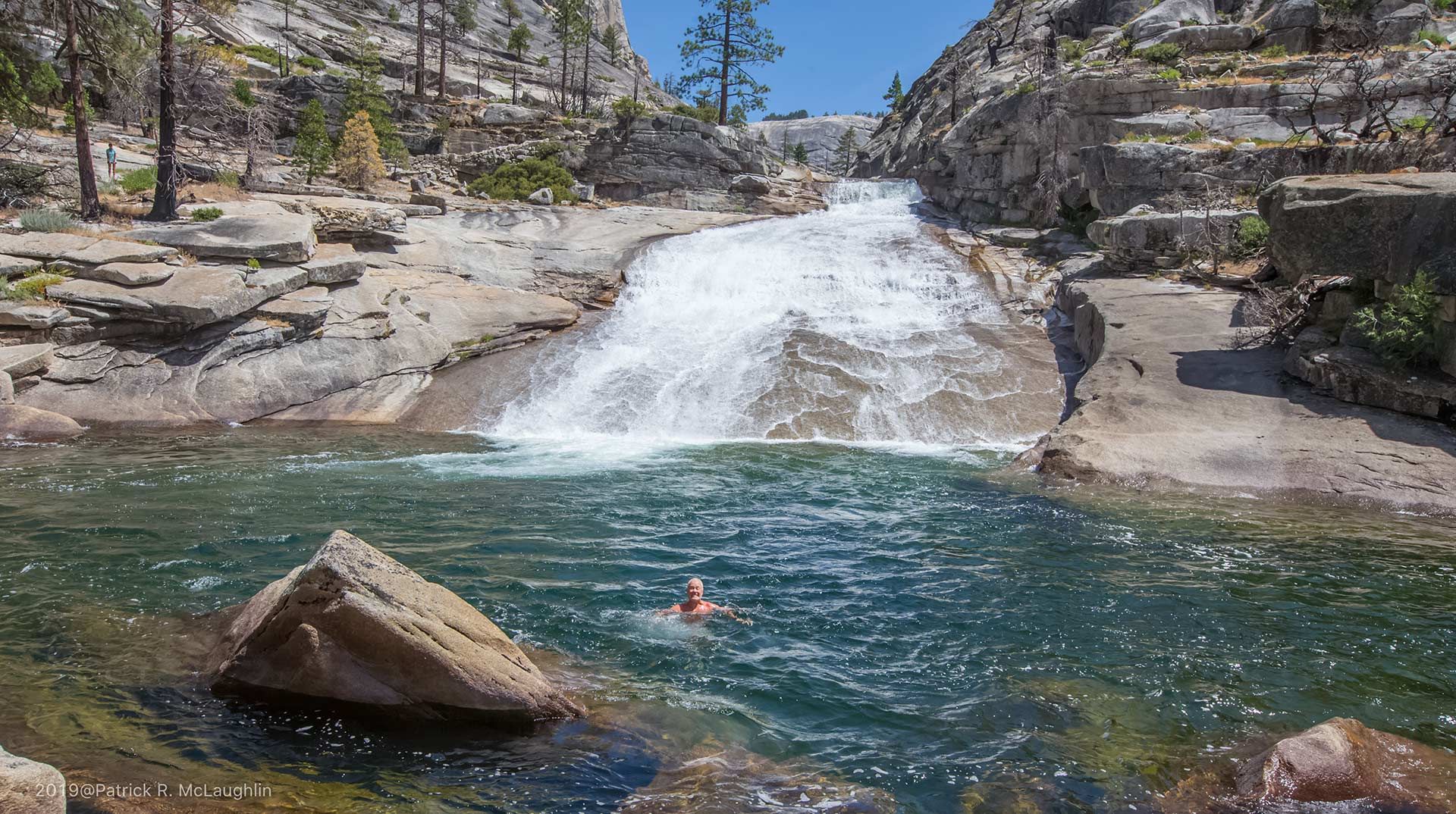 A person is swimming in a pool next to a waterfall.