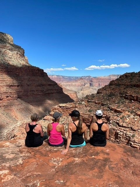 A group of women are sitting on a rock overlooking a canyon.