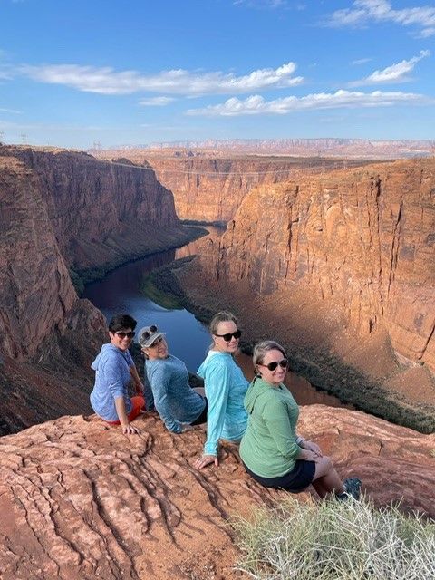 A group of people are sitting on the edge of a cliff overlooking a river.