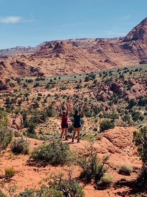 Two women are standing in the desert with their arms in the air.
