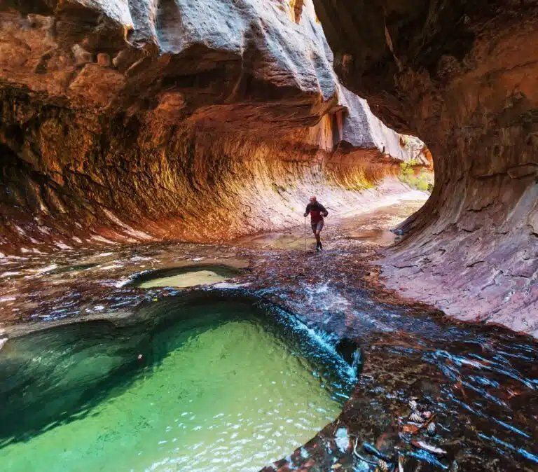 A person is running through a cave next to a pool of water