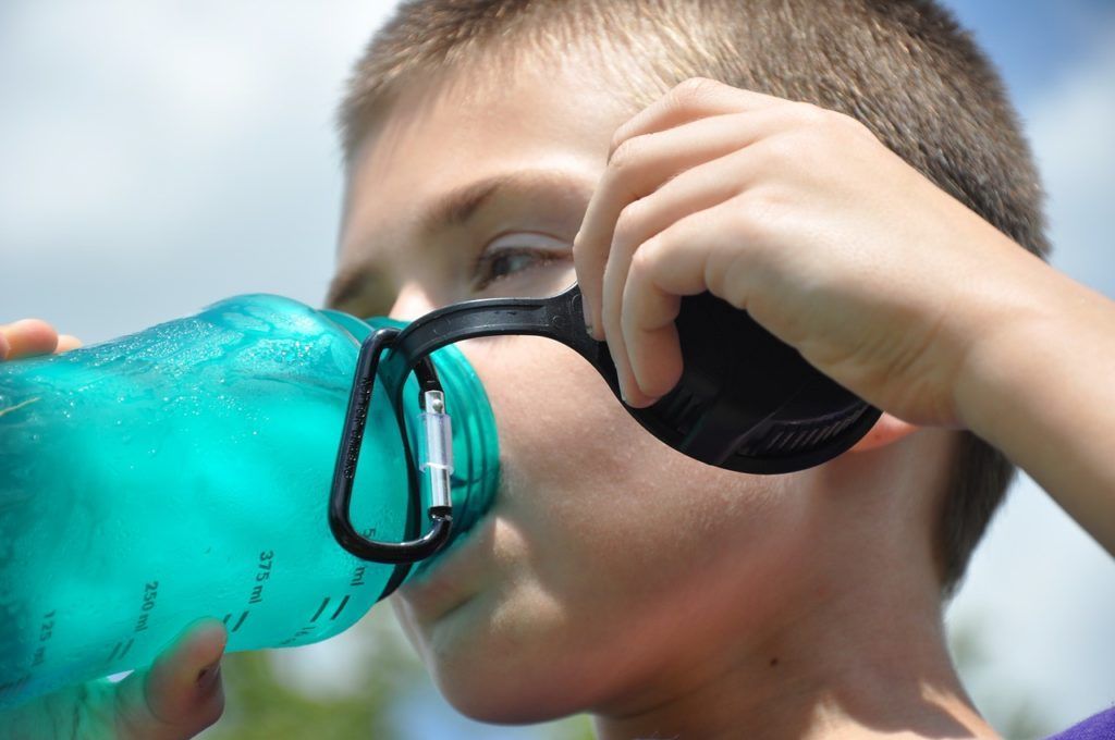 A young boy is drinking water from a blue bottle