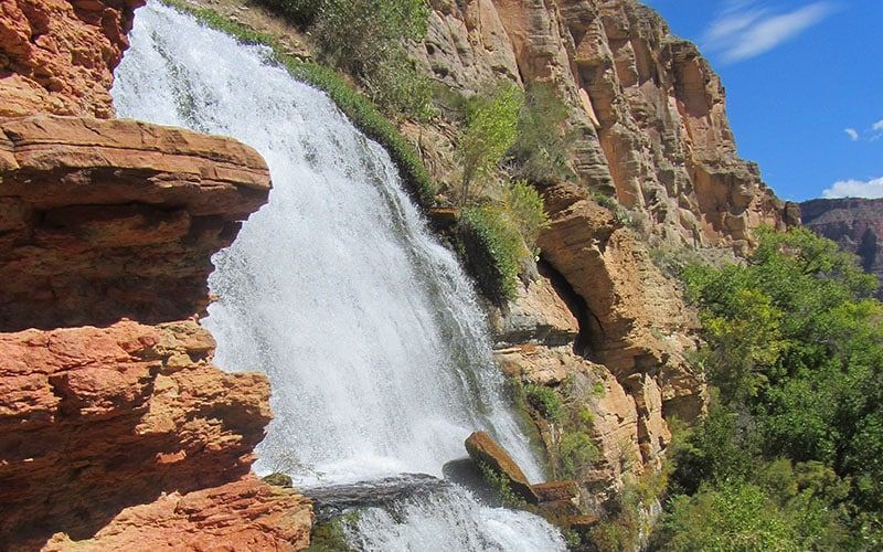 A waterfall is surrounded by rocks and trees on a sunny day