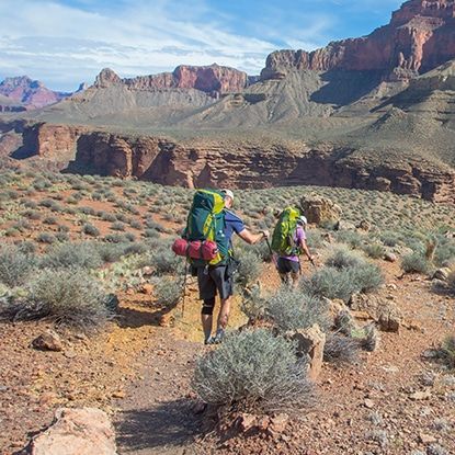 Two people are hiking in the desert with backpacks.