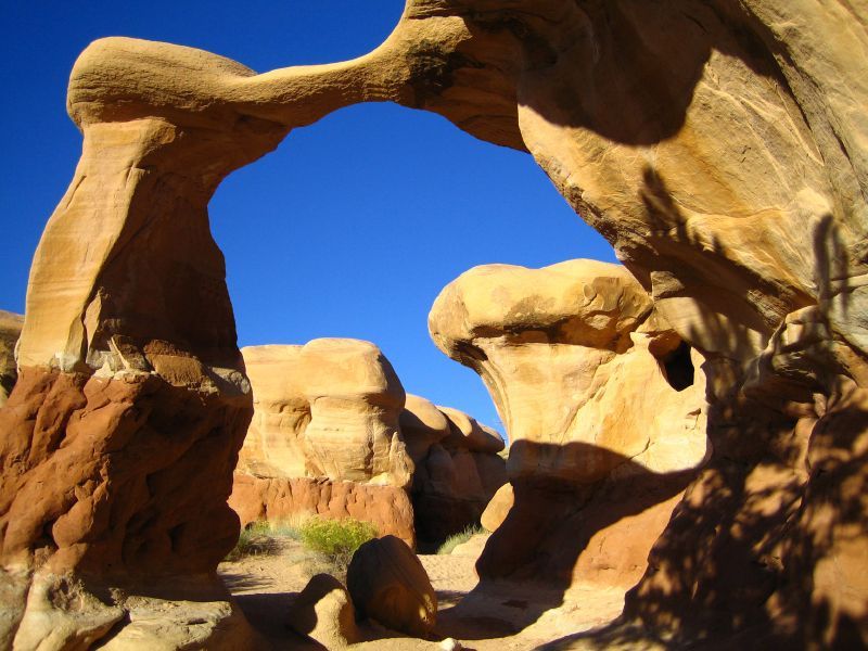 Natural sandstone arches and rock formations under a bright blue sky in a desert landscape