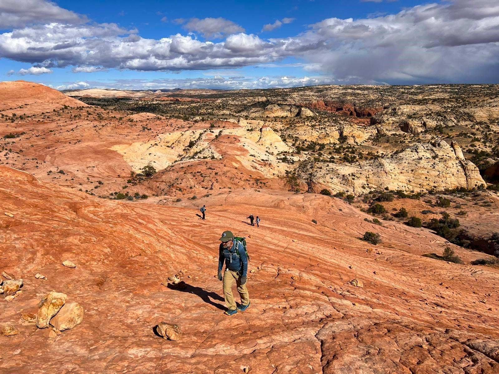 A man with a backpack is walking down a dirt path in the desert.