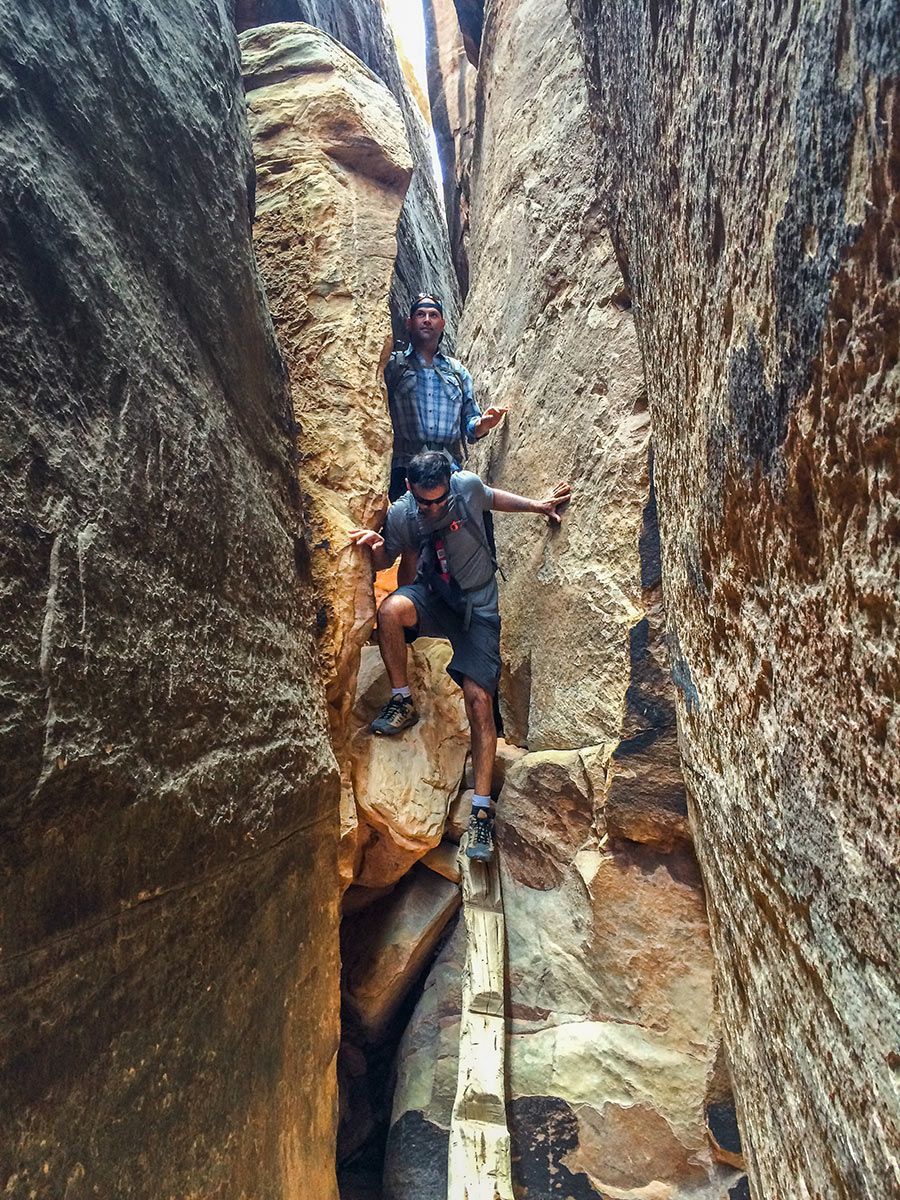 Two men are walking through a narrow canyon.