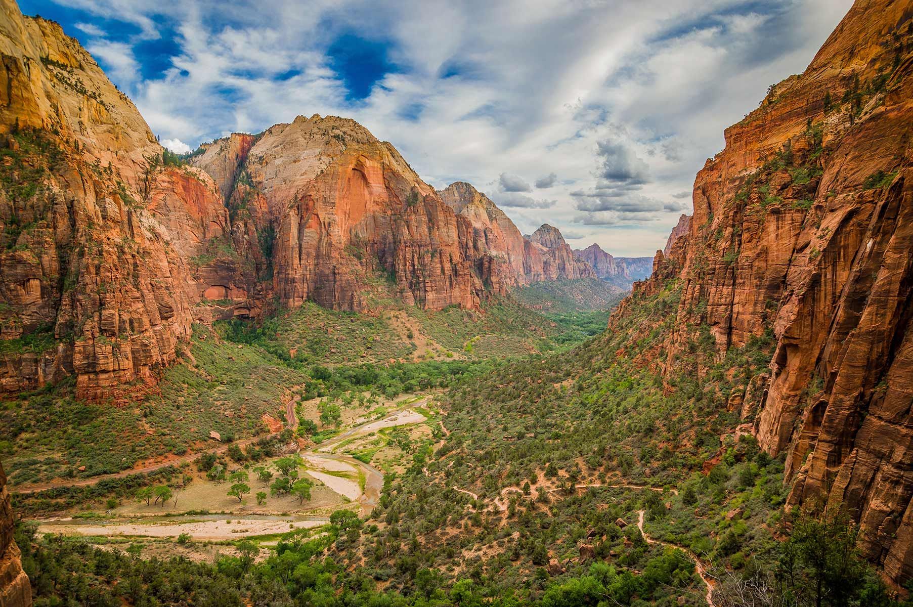 Red rock canyon with green vegetation and a winding river under a cloudy sky.