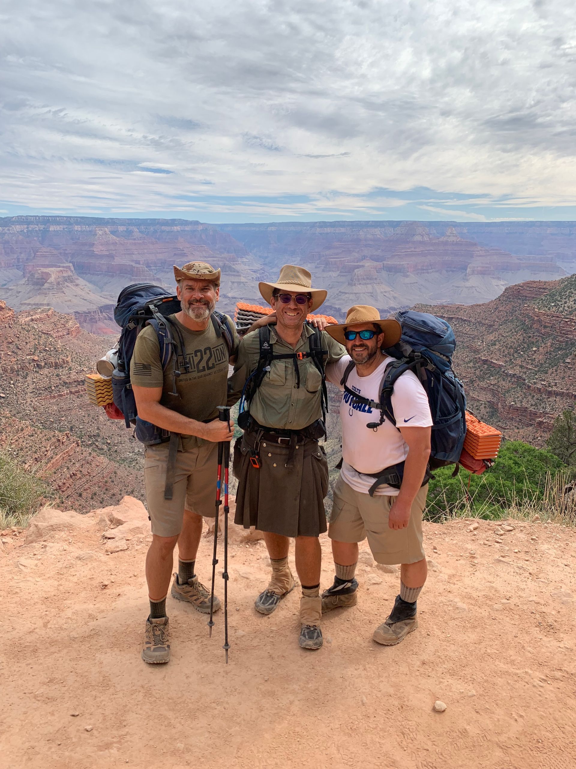 Three men are standing next to each other on top of a dirt hill.