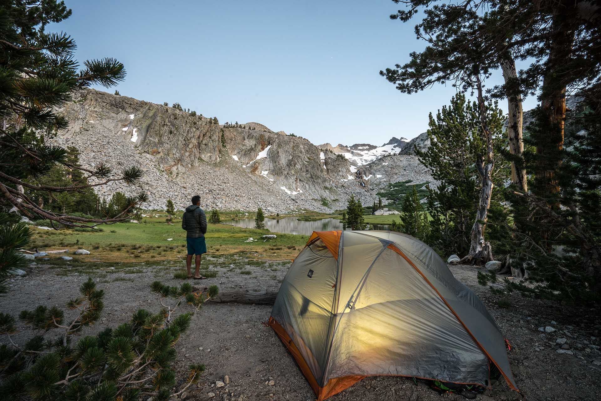 A man is standing in front of a tent in the mountains.