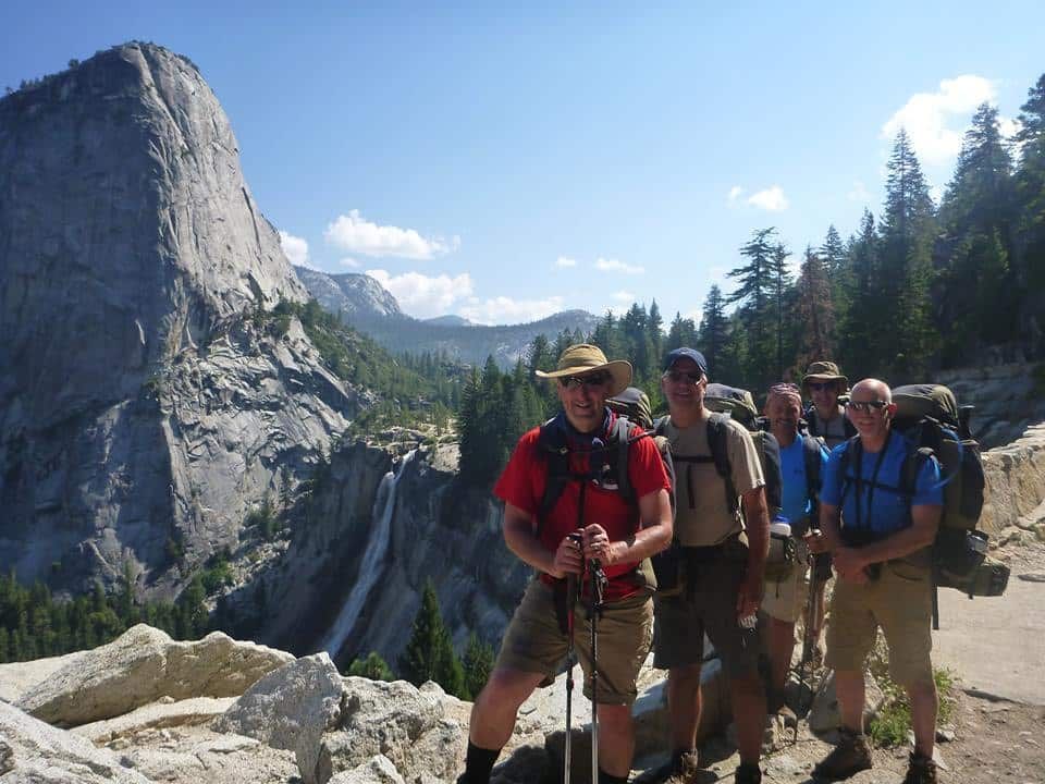 A group of men standing on top of a mountain with a waterfall in the background