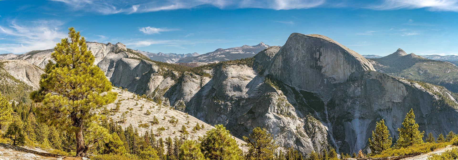 A panoramic view of a mountain range with trees in the foreground.