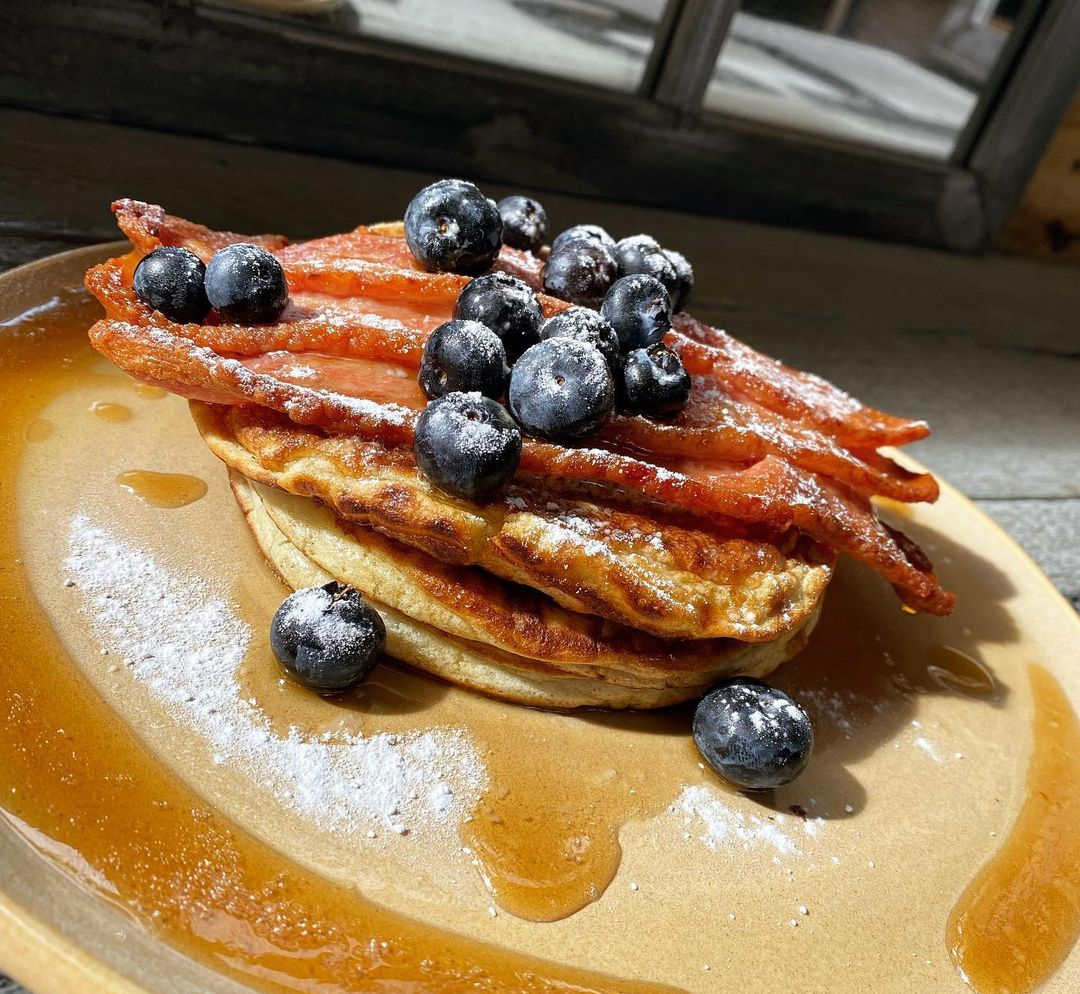 A stack of pancakes with blueberries and bacon on a plate