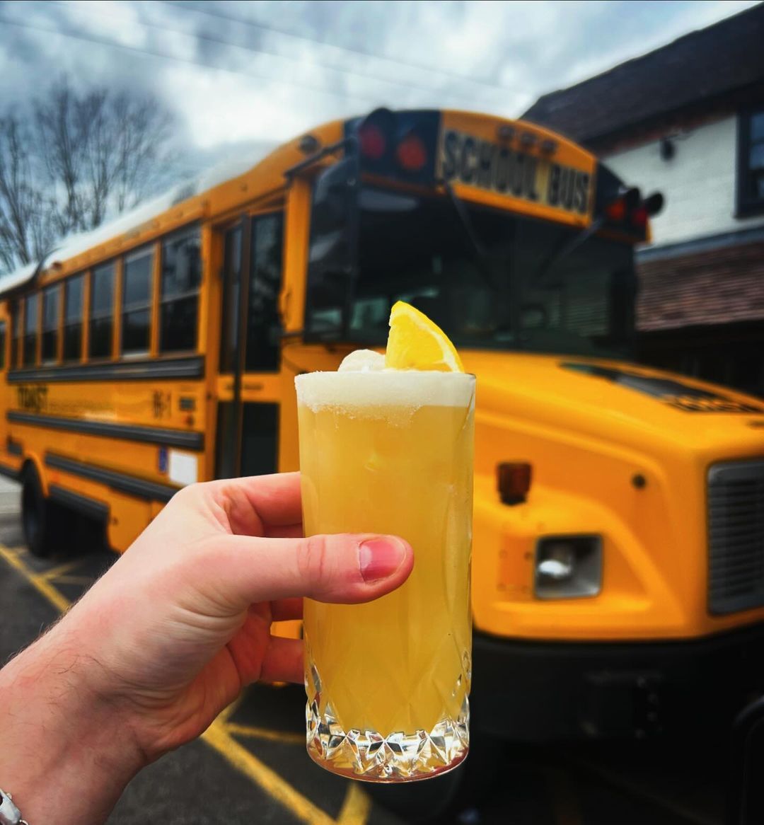 A person holding a cocktail  in front of the notorious TOAST Bus