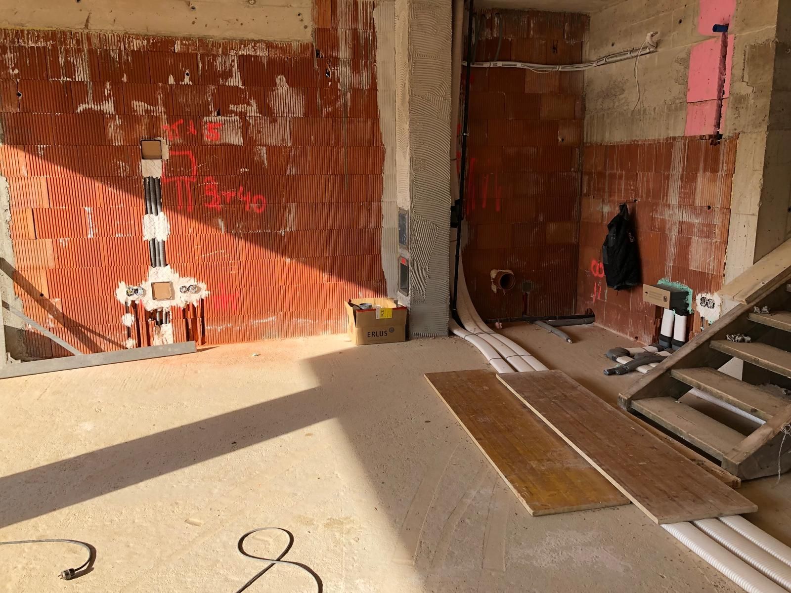 Innenbereich im Umbau mit freiliegenden roten Backsteinwänden, Betonboden und gestapelten Baumaterialien