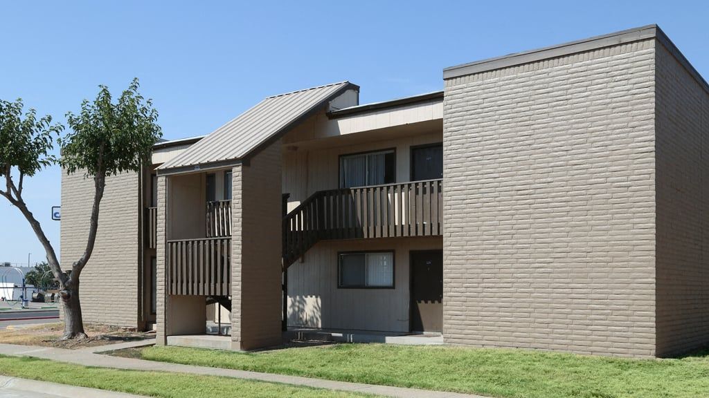 Two-story beige brick apartment building with exterior stairs, balconies, and surrounding trees at Brookview, offering apartments in Odessa, TX.