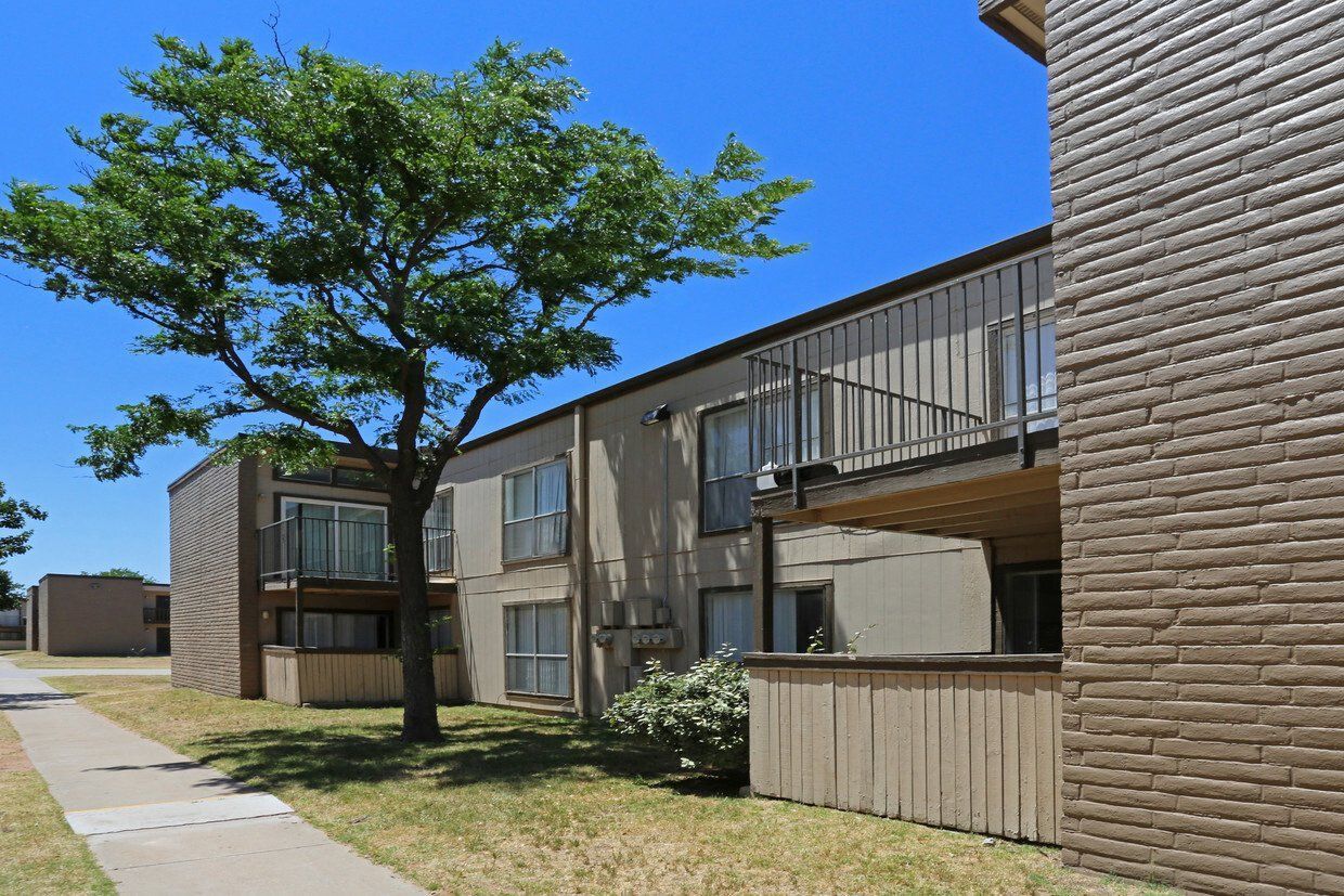 Exterior view of a two-story apartment building with balconies, a large tree, and a sidewalk at Brookview, offering apartments in Odessa, TX.