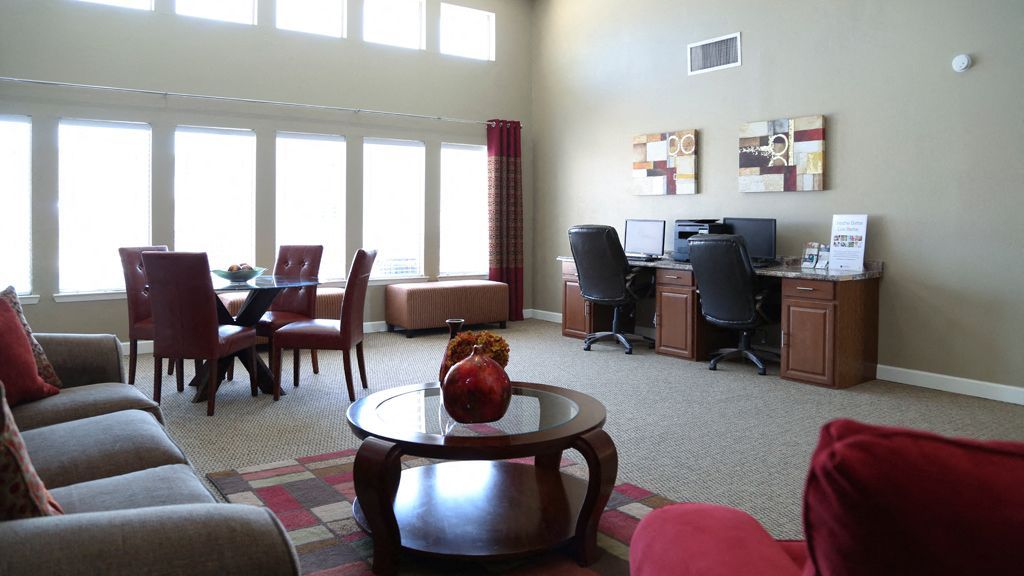 Community lounge with sofa, glass coffee table, dining set, and computer workstations at Brookview, offering apartments for rent in Odessa, TX.