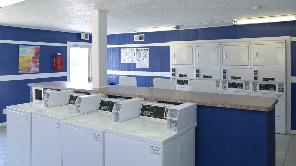 Laundry room with front-loading washers and stacked dryers against blue walls at Brookview, offering apartments for rent near Music City Mall in Odessa, TX.