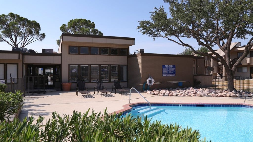 Outdoor pool area at apartment community with lounge chairs and a building in the background at Brookview, offering apartments for rent in Odessa, TX.