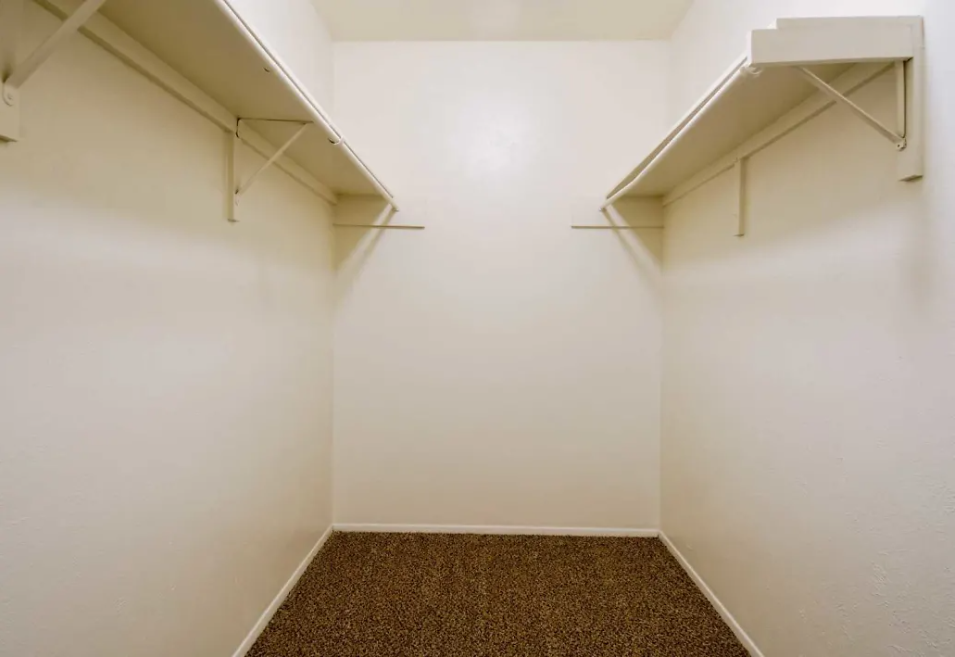 Empty walk-in closet with white walls, brown carpet, and white wire shelving along both sides at Brookview, offering apartments for rent near UTPB in Odessa, TX.