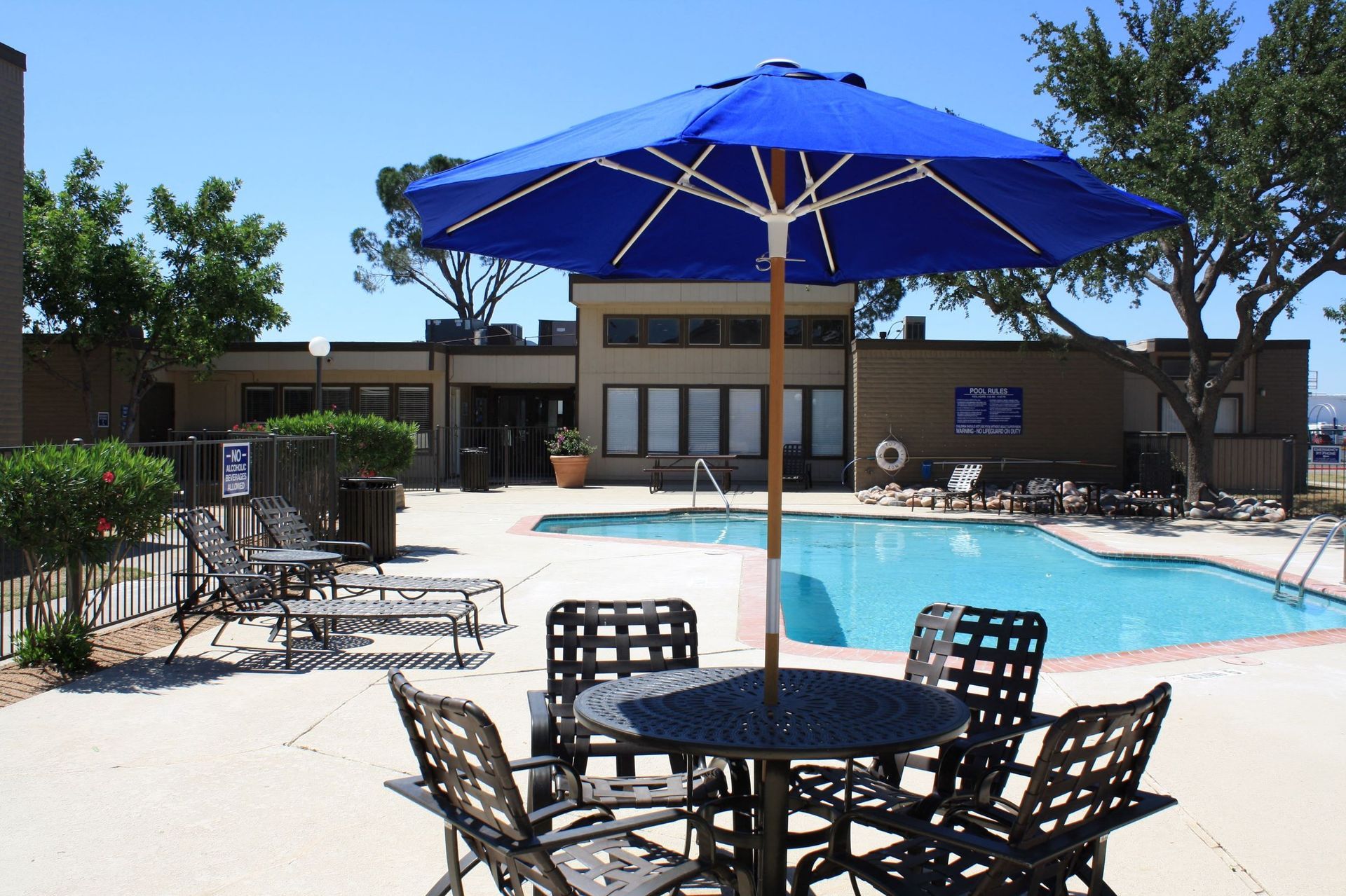 Outdoor apartment community pool area with lounge chairs and a large blue umbrella at Brookview, offering apartments in Odessa, TX.
