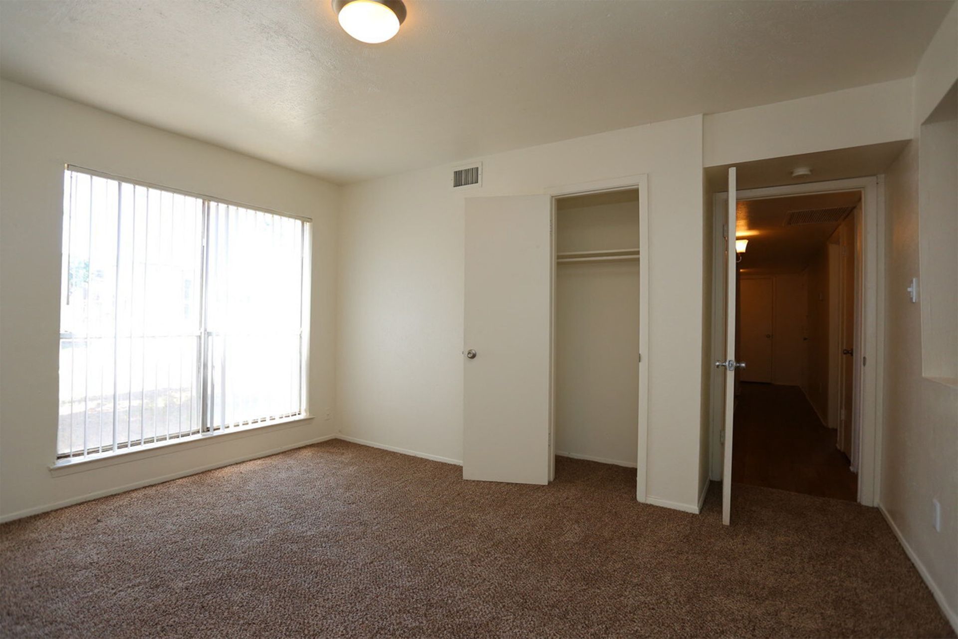 Bedroom with a large window and vertical blinds, carpet floor, and an open closet at Brookview, offering apartments for rent near UTPB in Odessa, TX.