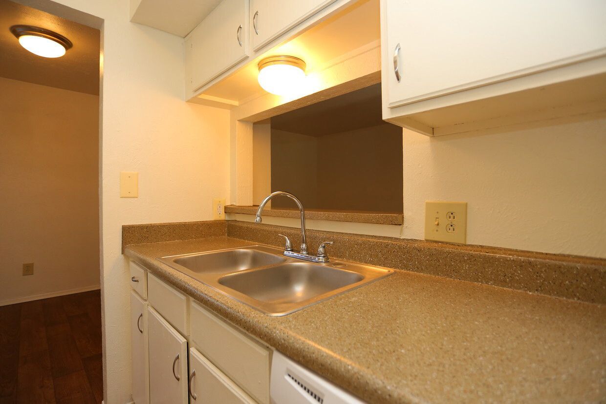 Kitchen with double sink, speckled beige countertops, white cabinets, and a pass-through window at Brookview, offering apartments for rent near Music City Mall in Odessa, TX.